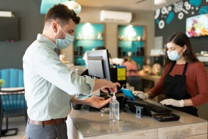Caucasian man applying disinfectant on hand at checkout counter in cafe during coronavirus crisis